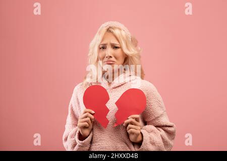 Signora infelice che tiene due metà del cuore di carta tagliato e piangendo, ritenendo ferito, passando con rottura romantica di rapporto Foto Stock