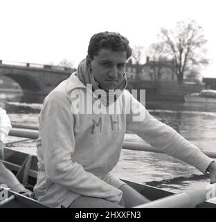 1960, storico, seduto in una barca a remi sull'acqua, il colpo della squadra della barca della Cambridge University, American Mark Hoffman di 1st & 3rd Trinity. Gli initali M.H sono ricamati sul suo top tuta in cotone. La famosa corsa di canottaggio universitaria, la Oxford & Cambridge Boat Race, si è svolta per la prima volta nel 1829 ed è un evento annuale sul Tamigi sul campo da campionato tra Putney e Barnes nel sud-ovest di Londra. Foto Stock
