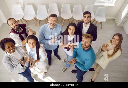 Un team diversificato di persone d'affari felici che si levano in piedi insieme, sorridendo e stringendo le mani Foto Stock