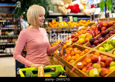 Donna anziana che usa il telefono delle cellule mentre acquista al supermercato Foto Stock