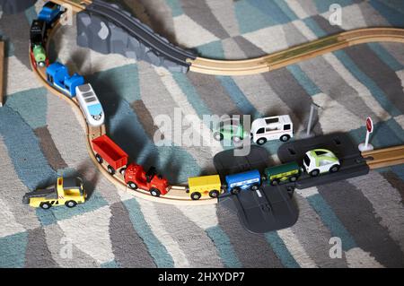Una collezione di treni giocattolo in plastica e locomotive con binari in legno su un pavimento in moquette a casa Foto Stock