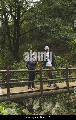 Colpo verticale di due uomini con bastoncini da trekking in piedi su un ponte di legno in una foresta Foto Stock