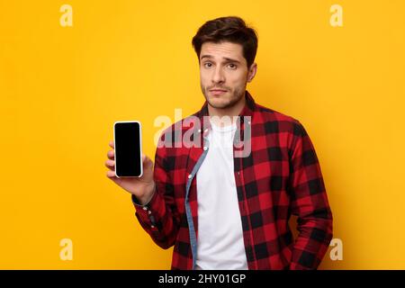 Un ragazzo triste che tiene in mano lo schermo dello smartphone vuoto Foto Stock