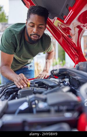 Uomo che lavora sotto il cofano controllo del livello dell'olio motore dell'auto sull'astina di livello Foto Stock