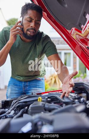 Uomo che guarda il motore dopo l'auto guasto chiamata recupero automatico sul telefono cellulare Foto Stock