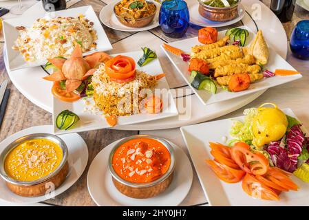 Set di piatti indiani con riso basmati e kashmir, curry rosso, cipolla bhaji, paneer palak, korma, pomodoro e lattuga Foto Stock