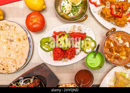 Set di piatti indiani, peperoni, salse, pomodori, curry rosso, cipolla bhaji, pollo tikka masala, samosa vegetale, spezie aromatiche, korma e lettu Foto Stock