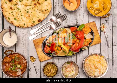 Set di deliziosi piatti indiani con curry piccante, pollo brasato tikka masala, riso basmati, curry di agnello brasato, spezie, posate, forcelle e peperoncino Foto Stock