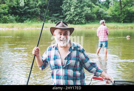 Uomini che pescano nel fiume durante la giornata estiva. Pesca felice pescatore in fiume tenendo canne da pesca. Trota su un gancio. Pesce sul gancio. Foto Stock