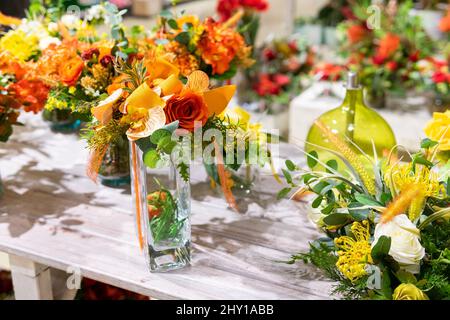 Abbondanza di fiori colorati in fiore con rose e foglie verdi in vasi di vetro posti sul tavolo in negozio floreale chiaro Foto Stock