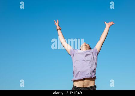 Uomo senza volto in t shirt in piedi con braccia e testa rialzate contro il cielo blu in natura nella giornata estiva soleggiata Foto Stock