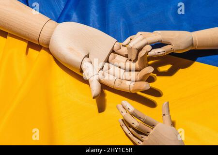 Dall'alto di tenere mano manichino in legno che rappresenta la tregua posta sulla bandiera nazionale Ucraina colorata con colori giallo e blu Foto Stock
