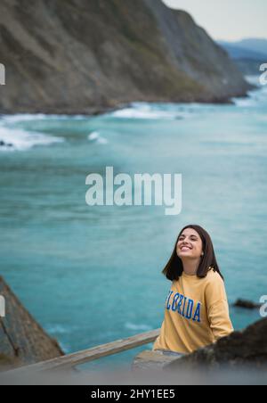 Attraente femmina in generale guardando lontano mentre si erge su una costa rocciosa vicino al mare ondulazione durante il viaggio nella zona costiera Foto Stock