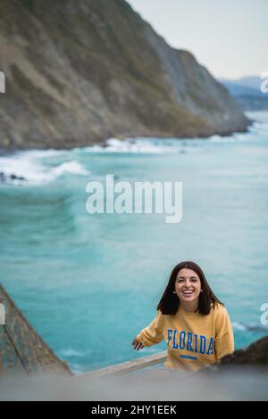 Attraente femmina in generale guardando la macchina fotografica mentre si trova sulla costa rocciosa vicino al mare ondulazione durante il viaggio nella zona costiera Foto Stock