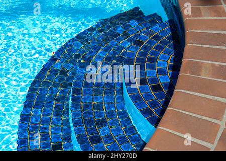 Primo piano di scalini in mosaico nella piscina con acqua blu limpida in una giornata di sole Foto Stock
