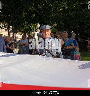 Suwalki, Polonia - 24 agosto 2019: Veterano militare in uniforme militare che detiene una grande bandiera polacca durante la celebrazione del centenario della liberazione Foto Stock