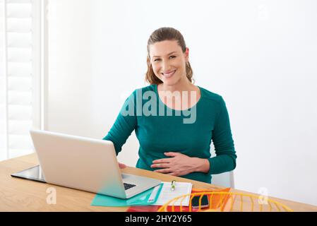 Incandescente e sano durante il congedo di maternità. Ritratto di una donna incinta seduta con il suo laptop a casa. Foto Stock