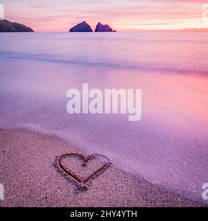 Cuore scolpito in sabbia su una spiaggia al tramonto Foto Stock