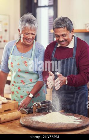 Quando si preparano alimenti, le mani potrebbero sporcarsi. Shot di una coppia matura felice divertirsi insieme mentre si prepara la pasta da zero a casa loro. Foto Stock