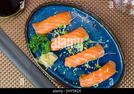 Deliziosa nigiri di salmone di prima qualità su piatto blu fatto a mano decorato Foto Stock