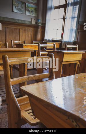 Ripresa verticale di un'aula nella scuola d'arte con scrivanie e sedie in legno e una grande finestra Foto Stock