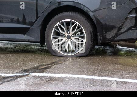 un'auto passeggeri con pneumatico sgonfio si trova sul marciapiede, bagnata dalla pioggia, in attesa di un'auto di servizio o di un autoriparatore, fuoco selettivo Foto Stock