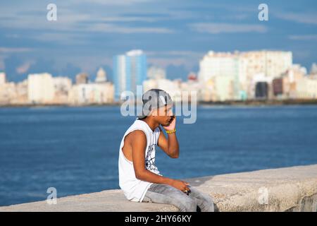 Il giovane cubano parla sul suo cellulare mentre siede sul Malacon a l'Avana, Cuba. Foto Stock