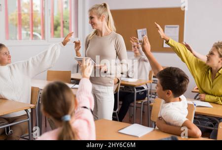 Gli allievi alzano le mani durante la lezione a scuola Foto Stock