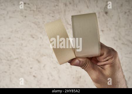 Primo piano di mano dell'uomo che maneggerà diversi tipi di nastri adesivi con fondo leggero per pareti Foto Stock