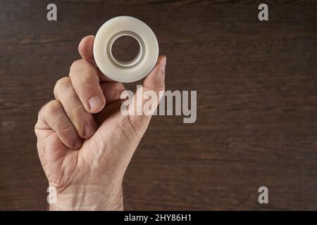 Primo piano di nastri adesivi per mano dell'uomo con fondo marrone Foto Stock