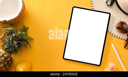 Tablet digitale bianco schermo mockup con frutti tropicali estivi, cappello da spiaggia e occhiali da sole su sfondo giallo. Composizione accessori vacanze estive Foto Stock