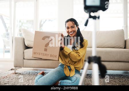 Abbiamo ricevuto nuova posta. Scatto corto di una giovane donna d'affari attraente seduta nel suo salotto e tenendo in mano una scatola di mistero mentre vlogging. Foto Stock