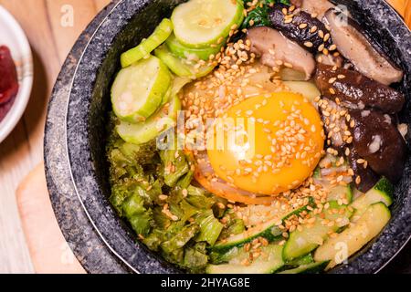 Bibimbap in una ciotola di pietra riscaldata nera, piatto tradizionale coreano - Bibimbap riso misto con verdure includono manzo e uova fritte, cibo giapponese caldo pentola Foto Stock