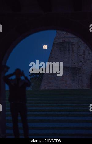 Vista posteriore verticale di un uomo sfocato scattando una foto della luna piena nel cielo della sera Foto Stock