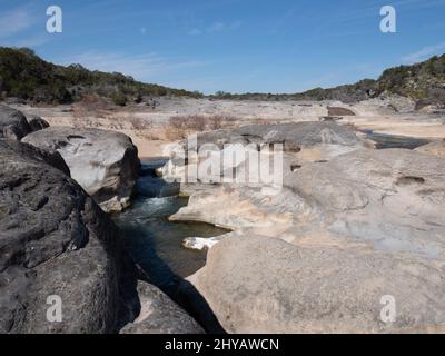 Il fiume Pedernales nel Pedernales Falls state Park vicino a Johnson City, Texas. Una piccola cascata di calcare è in primo piano e due escursioni Foto Stock