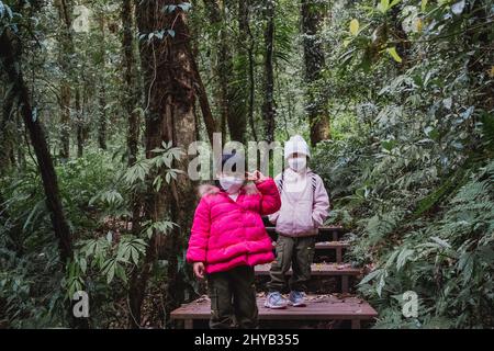 Bambini con zaini escursioni in natura con la famiglia. Due bambini in abiti invernali esplorano la foresta, giocano e imparano in natura. Una nuova normale li Foto Stock