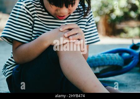 Triste bambina seduta a terra dopo essere caduta dalla sua bicicletta al parco estivo. Il bambino è stato ferito mentre guidava una bicicletta. Foto Stock