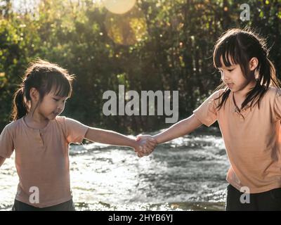 Due ragazze belle che tengono le mani felicemente giocando nel flusso. Le ragazze asiatiche stanno giocando nella cascata nella foresta. Attività ricreative attive con c Foto Stock