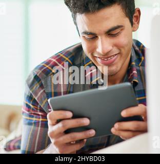 Controllare i feed dei social media. Girato di un bel giovane uomo usando il tablet mentre si rilassava sul divano a casa. Foto Stock