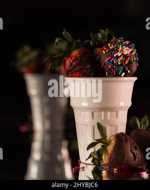 Shot verticale di fragole ricoperte di cioccolato con spruzzi in bicchieri di vetro bianco Foto Stock