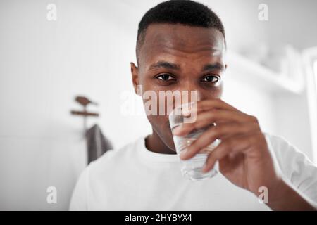 Bevi acqua e mantenersi in buona salute. Scatto corto di un giovane uomo che beve un bicchiere d'acqua a casa. Foto Stock