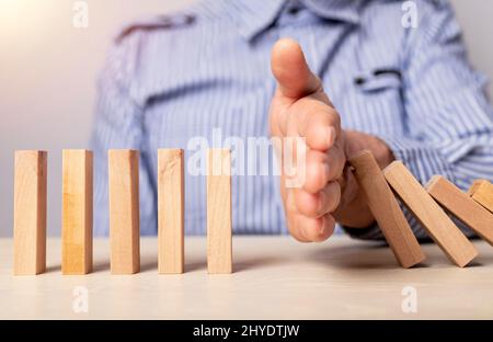 Il chiosco di mano dell'uomo d'affari protegge i blocchi di legno dalla caduta. Concetto di gestione del rischio e prevenzione delle crisi economiche. Foto di alta qualità Foto Stock