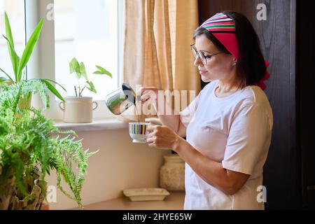 Donna di mezza età a casa in cucina che fa il caffè in un cezve di ferro Foto Stock