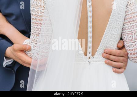 Bella bridesmaid vestire con numerosi pulsanti. Lo sposo abbraccia la vita della sposa, da vicino Foto Stock