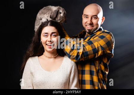 Ritratto di felice coppia caucasica giovane con simpatico coniglio orsato lop. Sfondo nero. Foto Stock