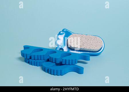 Accessori pedicure. Separatori di dita e pietra pomice su sfondo blu Foto Stock