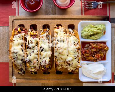 Tacos di pollo e formaggio cheddar su un tabellone di taco con salse sul lato Foto Stock