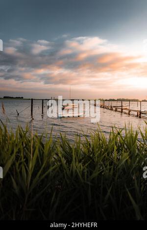 Colpo verticale da dietro l'erba delle barche nel mare sotto il cielo del tramonto bello in Danimarca Foto Stock