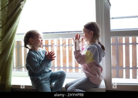 due ragazze stanno giocando patty-cake, seduti sul davanzale vicino alla grande finestra Foto Stock