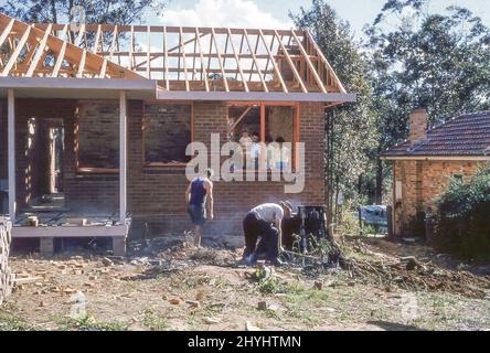 Sydney Australia 1959: Una giovane famiglia e un amico guardano mentre i costruttori lavorano sul nuovo cortile di una casa in mattoni rossi a Turramurra sulla sponda nord di Sydney in Australia. Nei giorni precedenti gli escavatori leggeri, i grandi ceppi di albero sono stati rimossi essendo messi sul fuoco e lentamente bruciati fuori. Grace Bros (grandi magazzini) Home Plans Service, istituito in associazione con il quotidiano Sunday Telegraph, Sydney, è stato lanciato nell'aprile 1954 e questa casa si basa su uno di questi piani. Vedere anche Alamy Image ID 2BWEYMX per la casa completa Foto Stock